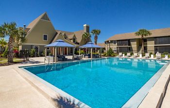 A large swimming pool with lounge chairs and umbrellas in front of a building